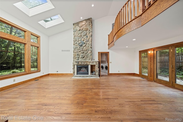 28190 Wildwood Trl, Farmington Hills, MI 48336 - unfurnished living room featuring washing machine and dryer, high vaulted ceiling, a skylight, a fireplace, and light wood finished floors