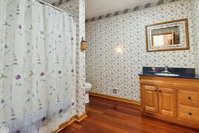 bathroom featuring visible vents, wallpapered walls, toilet, wood finished floors, and vanity