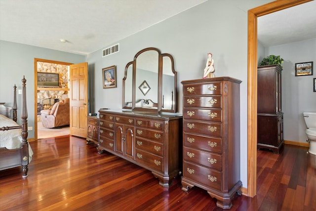 bedroom featuring dark wood-style floors, visible vents, a stone fireplace, and baseboards