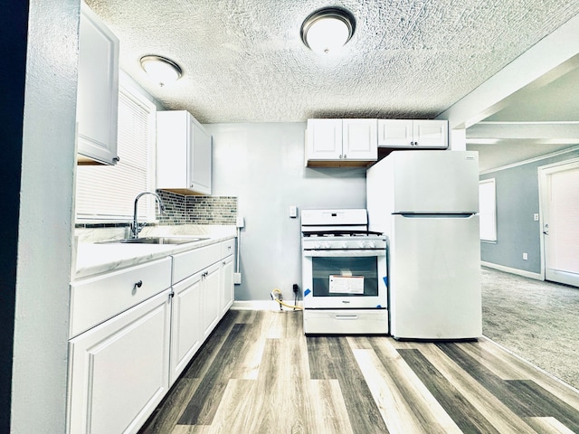 kitchen with white appliances, white cabinetry, backsplash, a sink, and wood finished floors