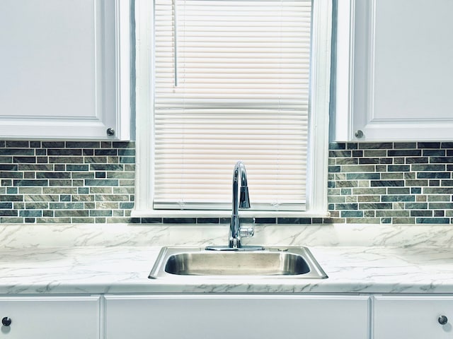 kitchen featuring tasteful backsplash, light stone countertops, white cabinetry, and a sink