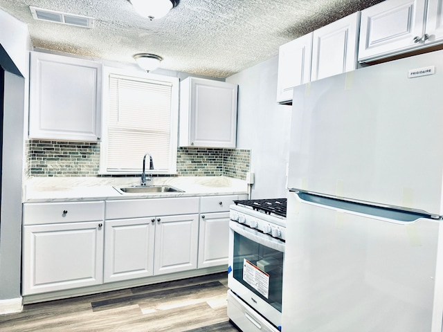 kitchen with a sink, visible vents, white cabinetry, and white appliances