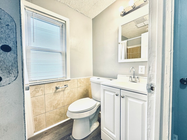 full bath featuring a textured ceiling, toilet, wood finished floors, wainscoting, and tile walls