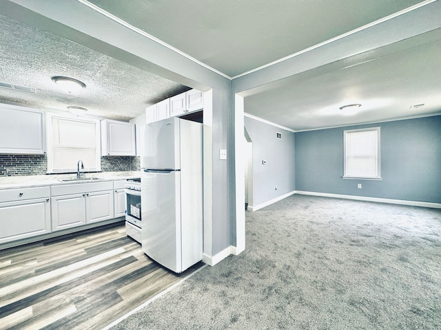 kitchen featuring stainless steel gas range oven, freestanding refrigerator, crown molding, white cabinets, and a sink