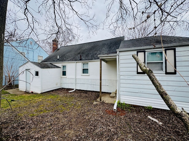 back of house featuring a shingled roof, a shed, an outdoor structure, and a chimney