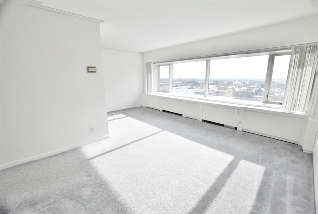 unfurnished room featuring a city view, light colored carpet, and baseboards