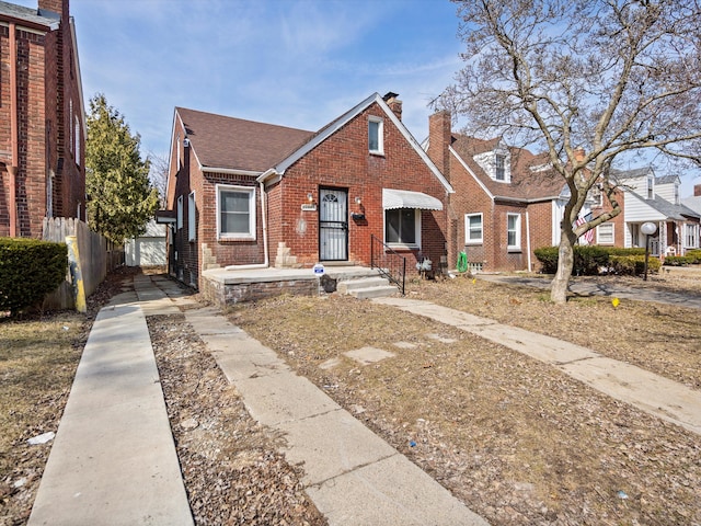 bungalow-style house featuring brick siding, a shingled roof, a chimney, and fence