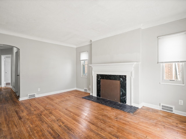 unfurnished living room featuring arched walkways, visible vents, and wood-type flooring