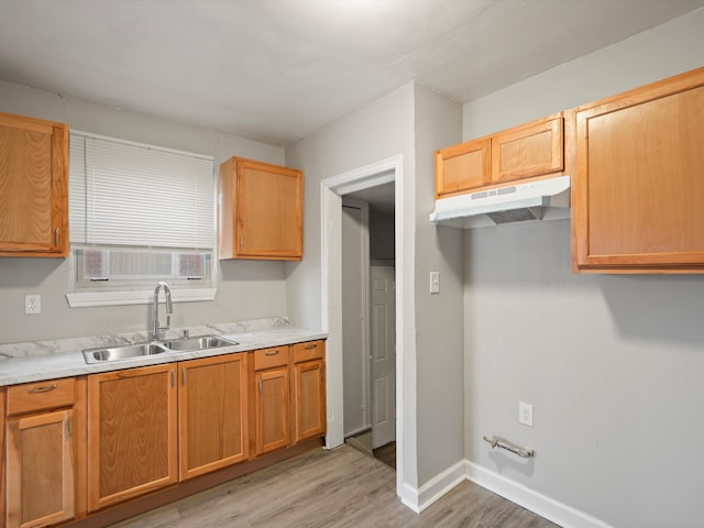kitchen with baseboards, under cabinet range hood, light countertops, light wood-style flooring, and a sink