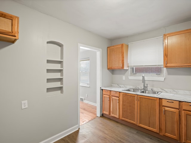 kitchen with a sink, light wood-type flooring, baseboards, and a healthy amount of sunlight