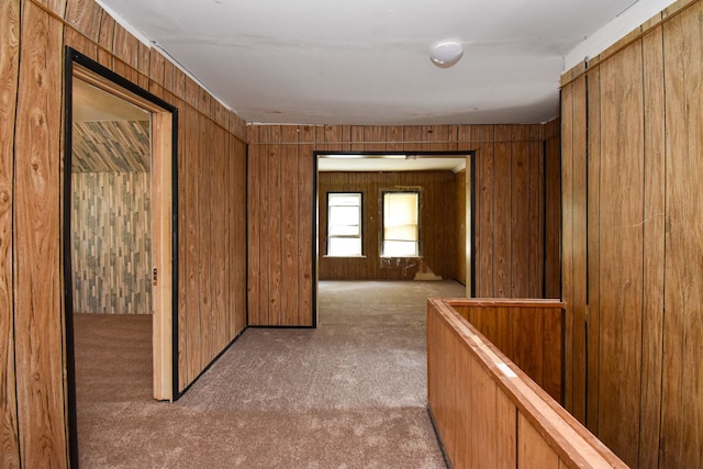 hall featuring wooden walls, an upstairs landing, and carpet floors