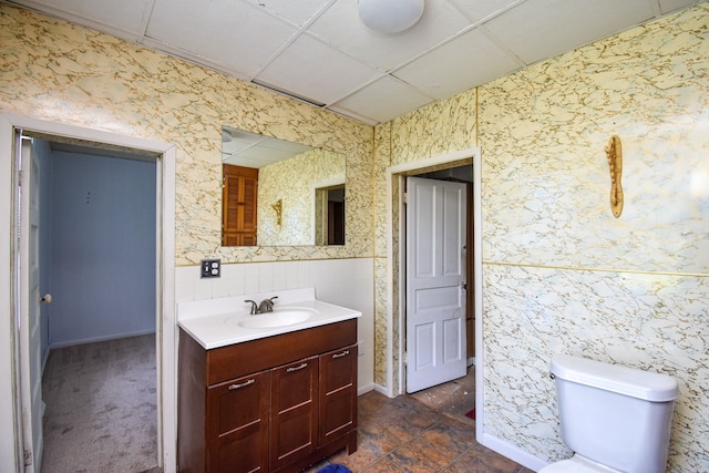 bathroom with vanity, toilet, a drop ceiling, and wallpapered walls