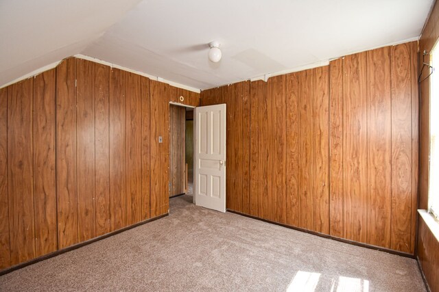 unfurnished room featuring lofted ceiling, wood walls, and carpet floors