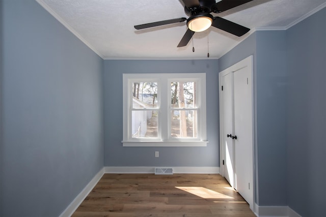 unfurnished bedroom with baseboards, wood finished floors, visible vents, and ornamental molding