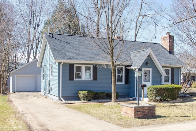 view of front of home featuring an outbuilding, a chimney, driveway, and a shingled roof