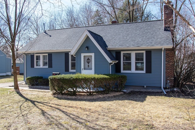 view of front facade with a chimney, a shingled roof, and a front lawn
