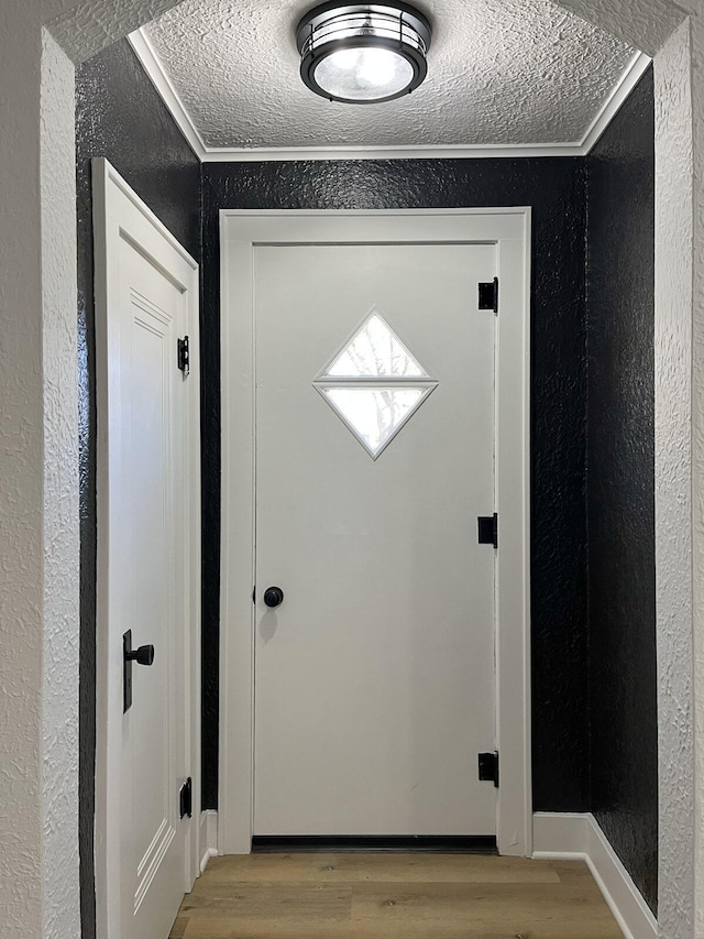 doorway to outside with wood finished floors, a textured wall, and ornamental molding