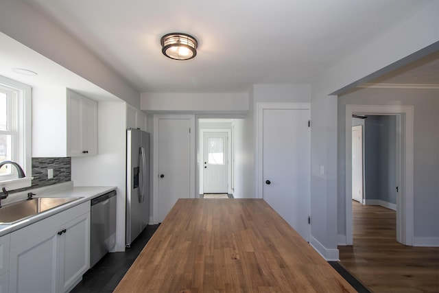 kitchen with dark wood-style flooring, butcher block countertops, decorative backsplash, stainless steel appliances, and a sink