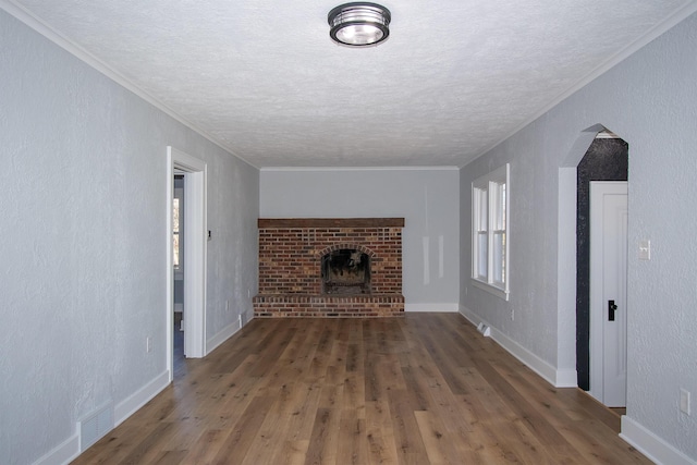 unfurnished living room featuring visible vents, wood finished floors, arched walkways, crown molding, and a textured wall
