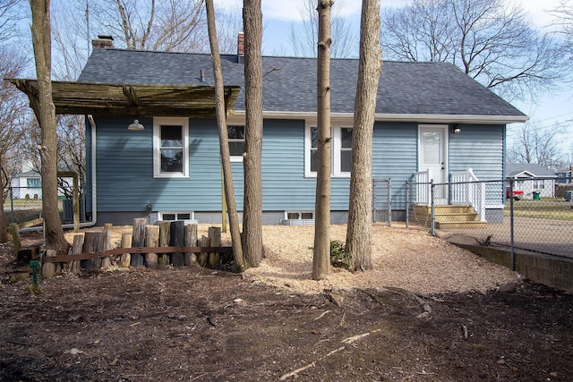 rear view of property with a chimney, a shingled roof, and fence