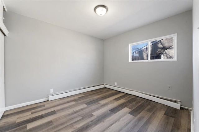 empty room with a baseboard heating unit, baseboards, and wood finished floors
