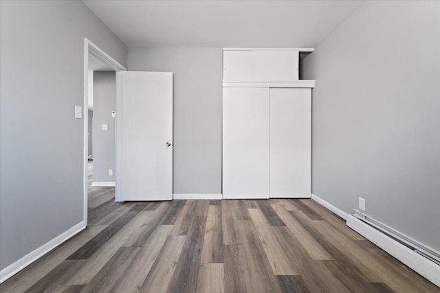 unfurnished bedroom with a baseboard heating unit, baseboards, a closet, and wood finished floors