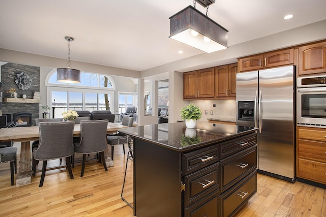 kitchen featuring tasteful backsplash, decorative light fixtures, open floor plan, light wood-type flooring, and appliances with stainless steel finishes