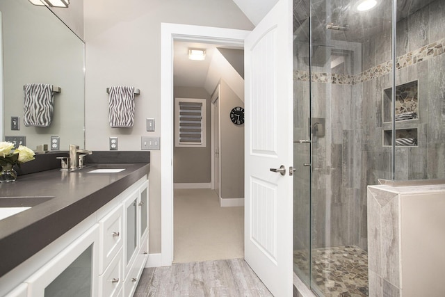 bathroom featuring a shower stall, baseboards, double vanity, wood finished floors, and a sink