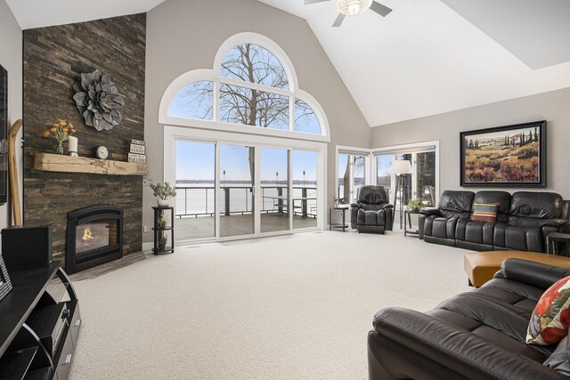 carpeted living area featuring a stone fireplace, high vaulted ceiling, and ceiling fan