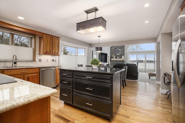 kitchen featuring light stone counters, brown cabinetry, a sink, stainless steel appliances, and light wood-type flooring