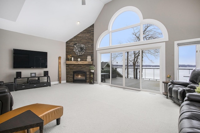 living area featuring baseboards, carpet floors, high vaulted ceiling, ceiling fan, and a stone fireplace