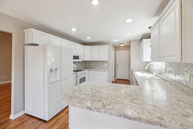 713 Mary Ann Dr, Holly, MI 48442 - kitchen with decorative backsplash, a sink, a peninsula, white appliances, and light wood-style flooring