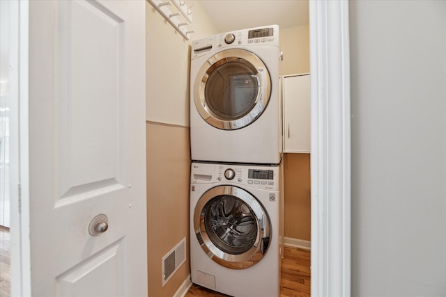 713 Mary Ann Dr, Holly, MI 48442 - clothes washing area featuring stacked washer / drying machine, wood finished floors, and visible vents
