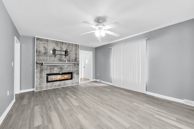unfurnished living room with visible vents, baseboards, ceiling fan, a tiled fireplace, and wood finished floors