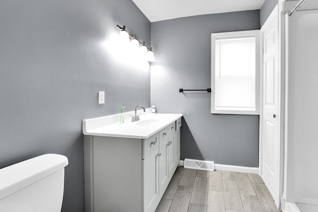 bathroom featuring visible vents, baseboards, toilet, wood finished floors, and vanity