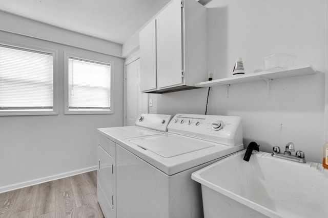 clothes washing area featuring a sink, washing machine and dryer, cabinet space, light wood finished floors, and baseboards