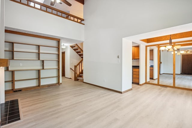 131 E Jolly Rd Unit E6, Lansing, MI 48910 - unfurnished living room with a chandelier, light wood-style floors, a ceiling fan, stairs, and a high ceiling