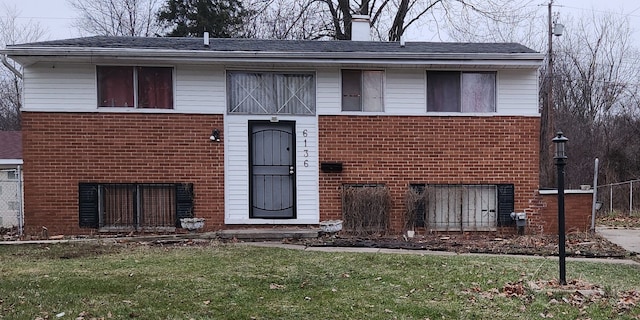 split foyer home featuring brick siding, a chimney, and a front lawn