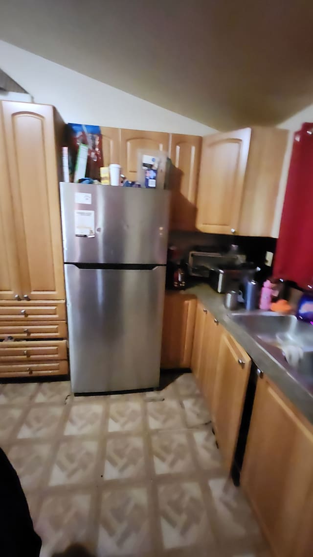 kitchen with dark countertops, light floors, freestanding refrigerator, and a sink