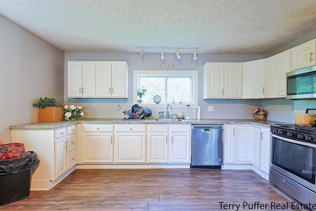 kitchen featuring stainless steel appliances, a sink, white cabinets, dark wood finished floors, and a textured ceiling