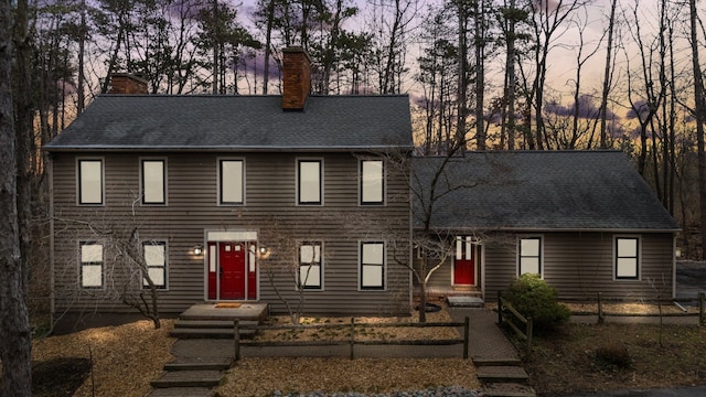 colonial house with a chimney, fence, and roof with shingles