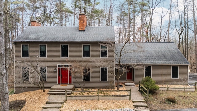 colonial home featuring a chimney, fence, and roof with shingles