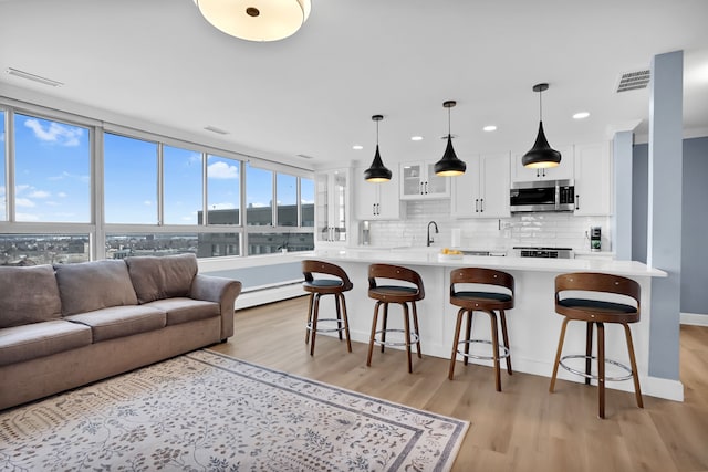 kitchen with baseboard heating, white cabinets, light wood-style floors, light countertops, and stainless steel microwave