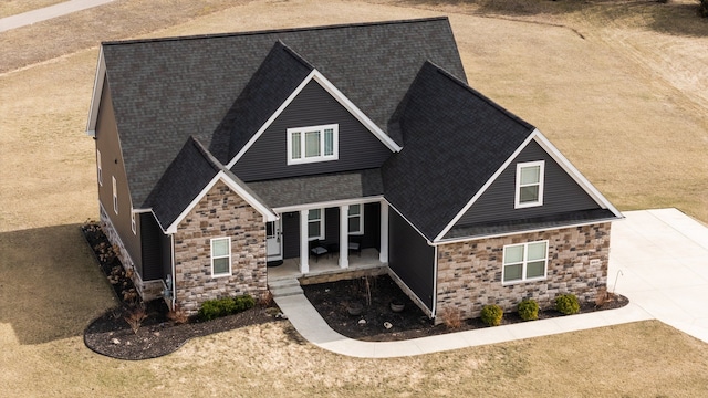 craftsman house with a porch, roof with shingles, and stone siding
