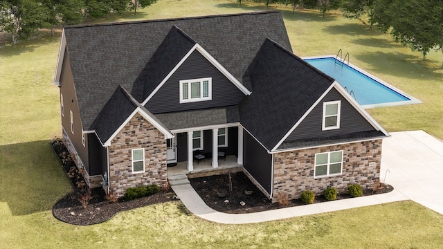 craftsman house with roof with shingles, a patio area, stone siding, and a front lawn
