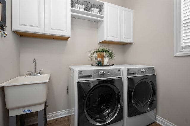 washroom featuring wood finished floors, baseboards, separate washer and dryer, a sink, and cabinet space