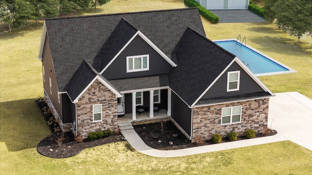 view of front of house featuring a front lawn, roof with shingles, and stone siding