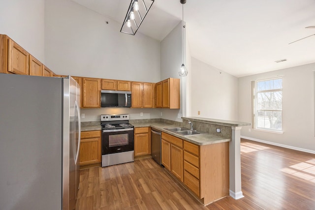 kitchen featuring baseboards, light wood finished floors, a peninsula, a sink, and stainless steel appliances