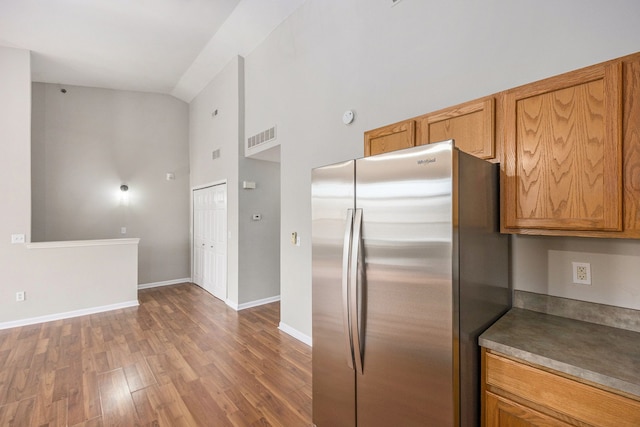 kitchen featuring brown cabinetry, wood finished floors, visible vents, baseboards, and freestanding refrigerator