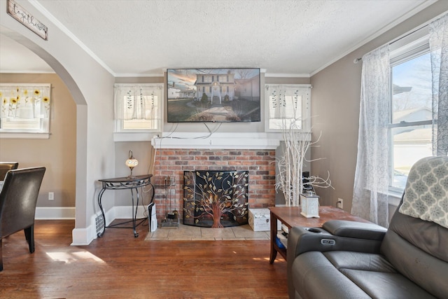 living area featuring a brick fireplace, arched walkways, crown molding, and wood finished floors